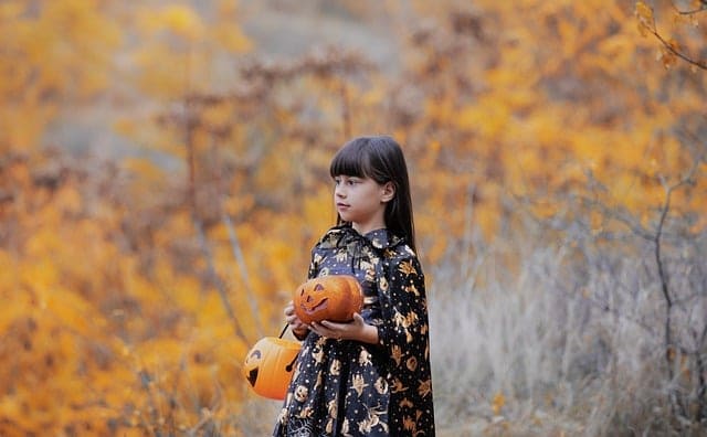 Petite fille déguisée en sorcière qui tient une citrouille d'Halloween entre ses mains