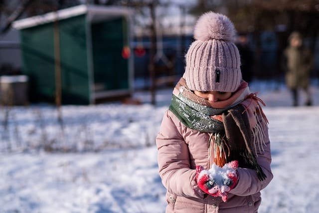 Enfant avec manteau, écharpe et bonnet qui tient de la neige entre ses mains