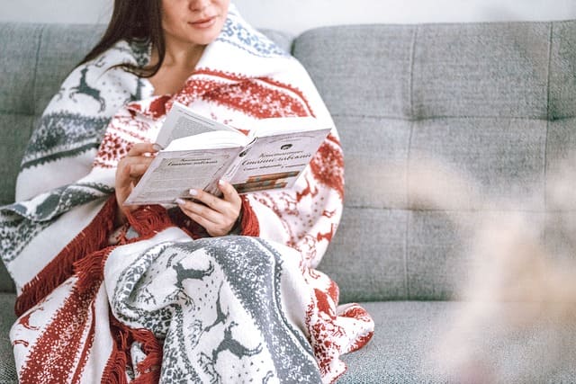 Femme en train de lire sur le canapé, enveloppée dans un plaid de Noël